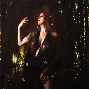 Capa do single “Vestida de Estrelas” de Ana Leana, com a artista em pé, cercada por brilhos dourados que lembram estrelas no céu noturno.